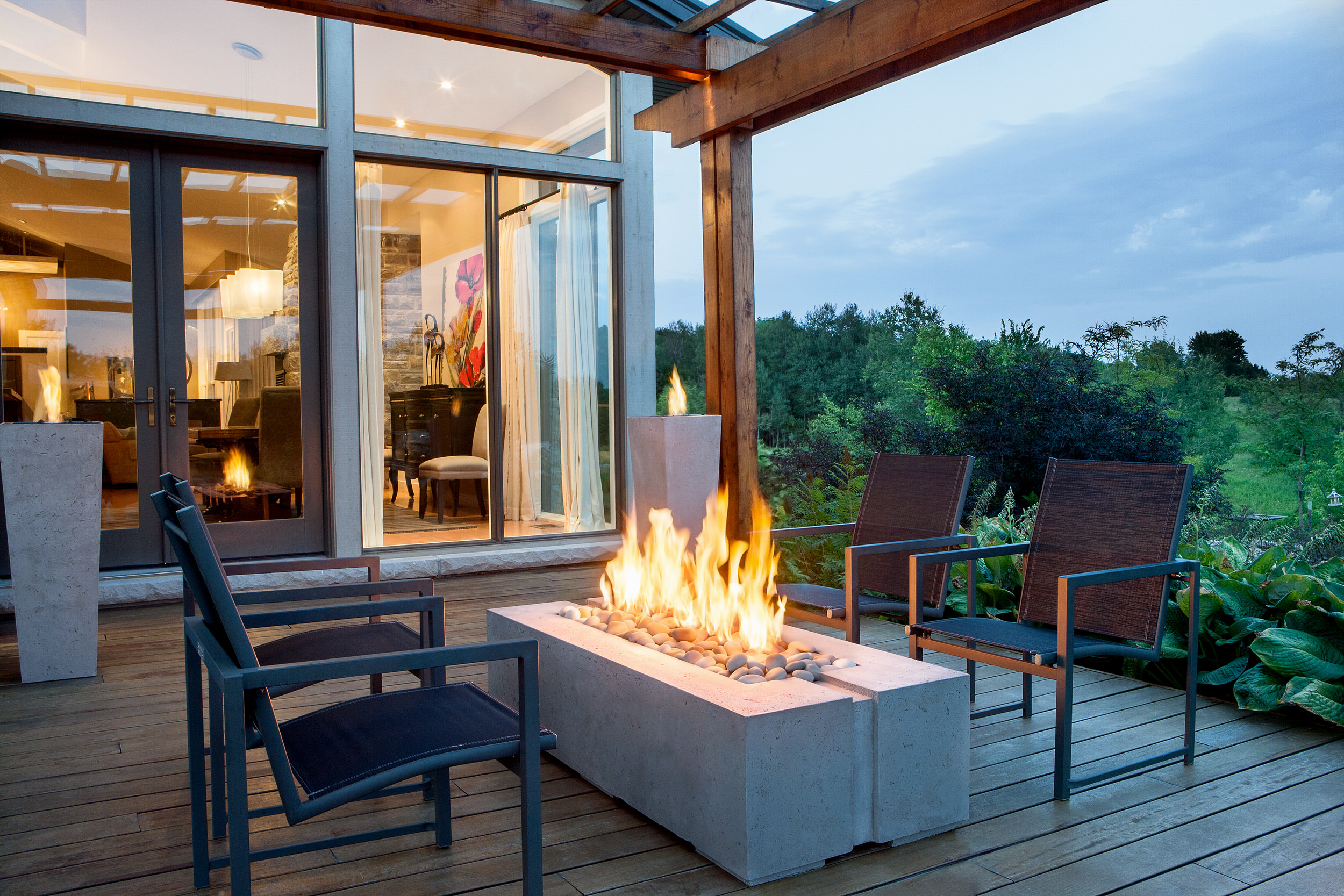 Four outdoor chairs around a rectangular, lit Dekko fire pit from the Avera collection on wooden decking.