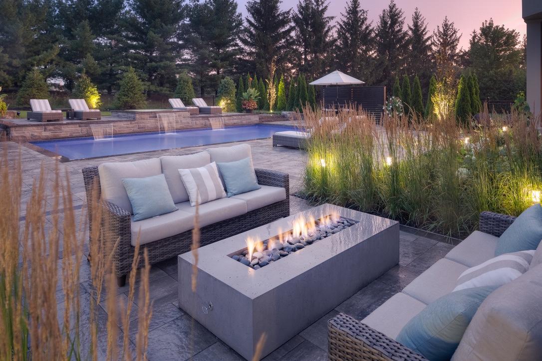 A Dekko concrete fire pit in between two couches on a patio of a home with a pool.