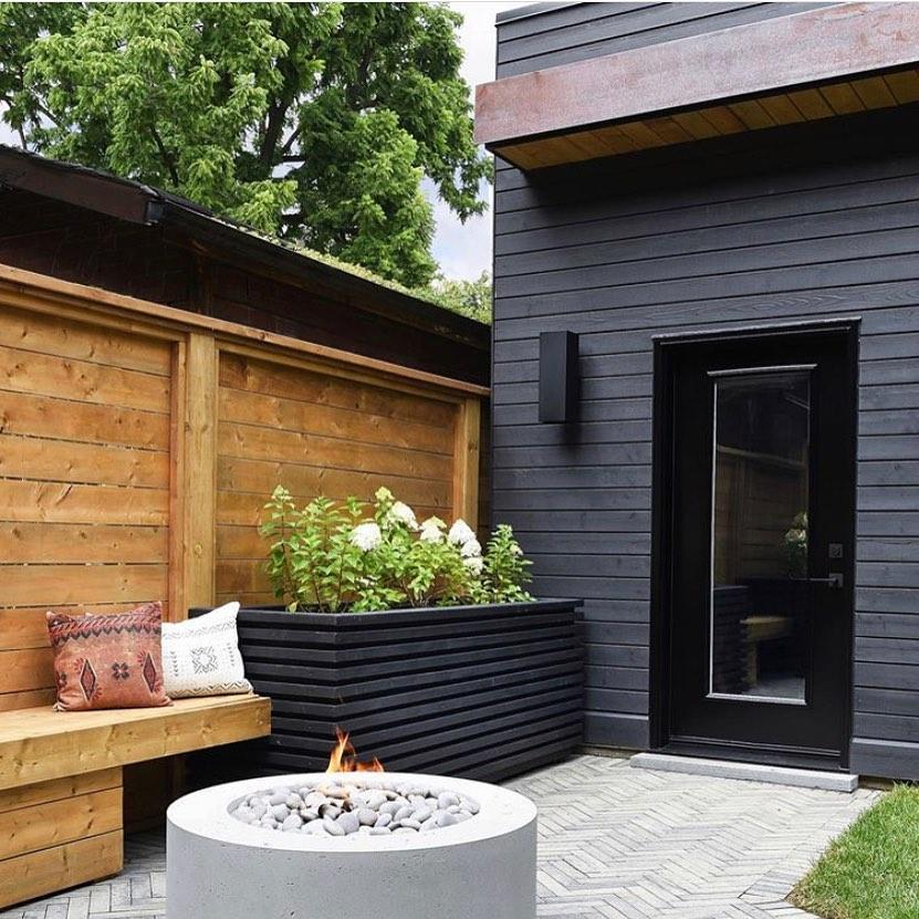 A small outdoor space with a wooden bench, Dekko Belmont fire pit and painted wooden box with plants.