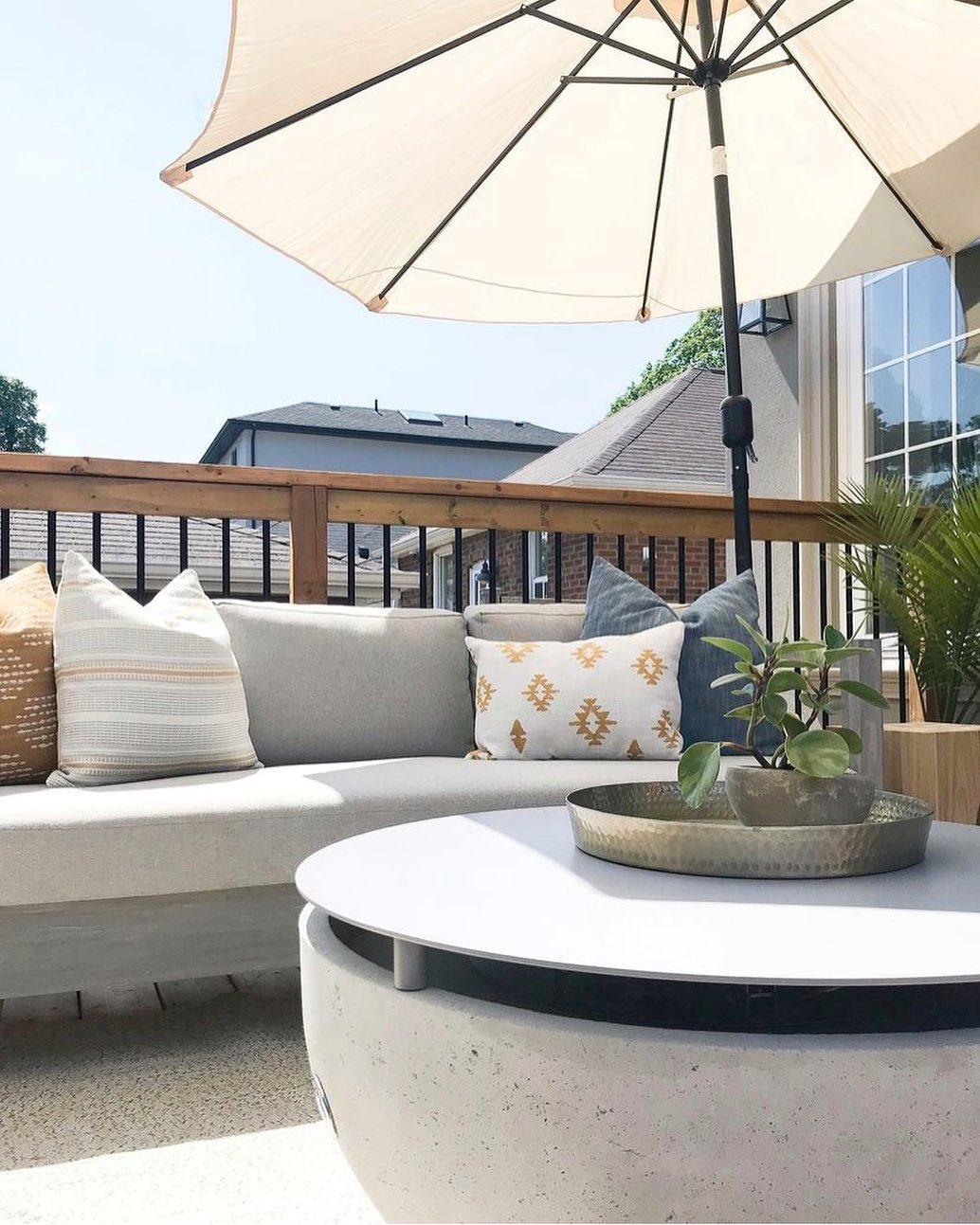 An outdoor space with a sofa, cushions, parasol and a Dekko Serenade firepit with added tabletop cover.