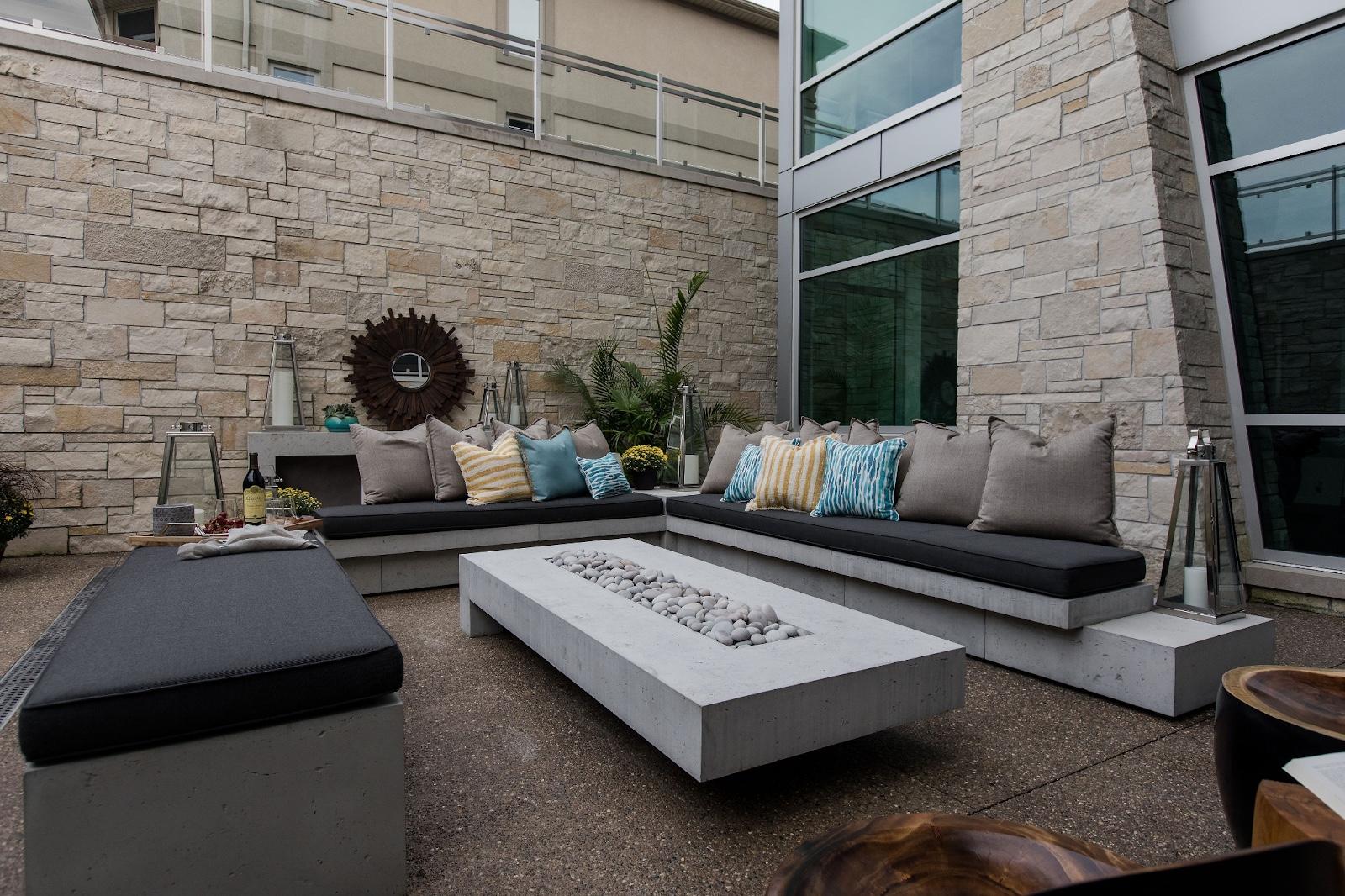 This outdoor sitting area has three sofas. There is a large rectangular fire pit in the middle of the sitting area.