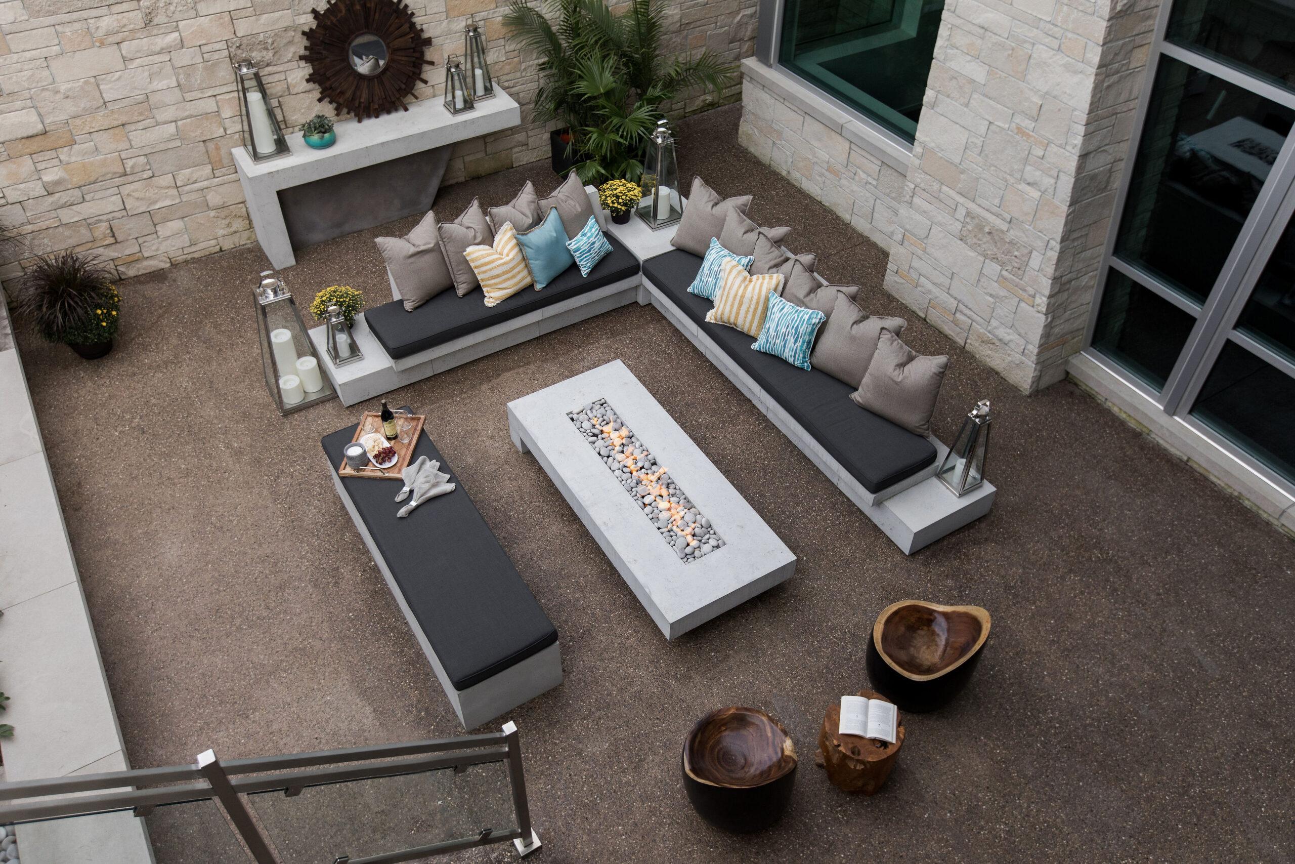 Dekko’s lightweight concrete fire pit and a concrete table with three benches surrounding it outside full of pillows.